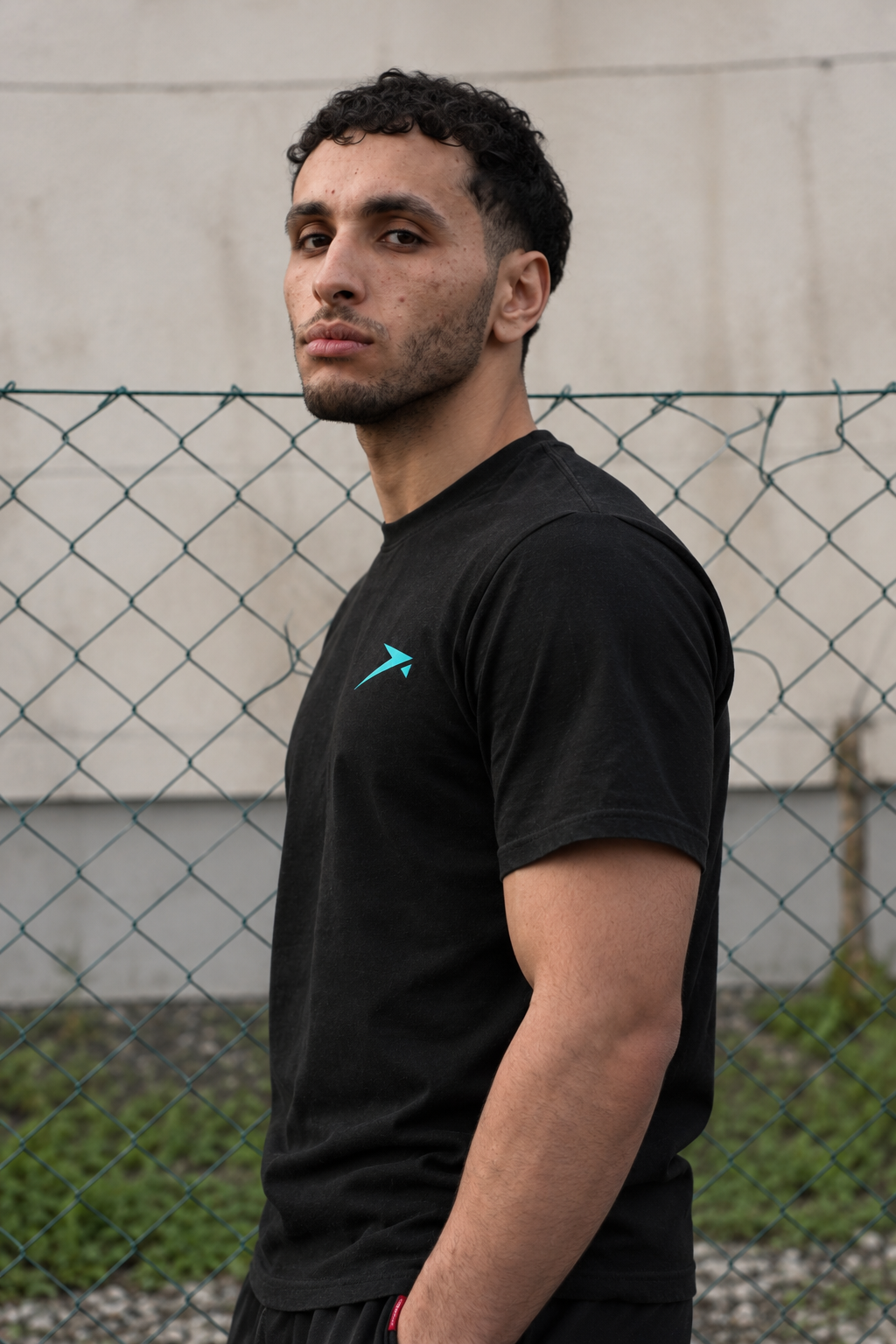 Side profile in the black Beldi Dept. Performance T-Shirt with aquamarine logo