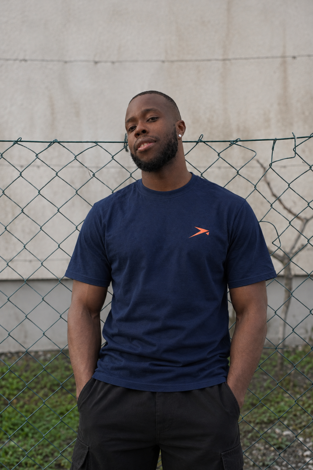 Urban portrait at a wire fence in the navy Beldi Dept. Performance T-Shirt